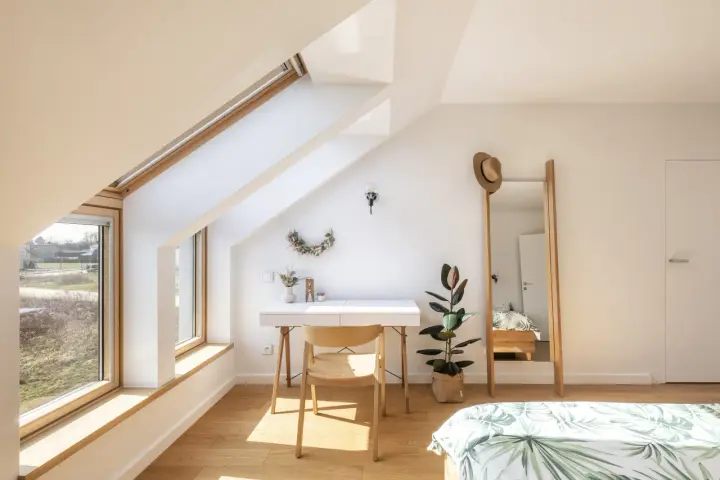 Angolo studio mansardato inondato da la luce più naturale. Scrivania, sedia in legno, specchio alto e pianta.