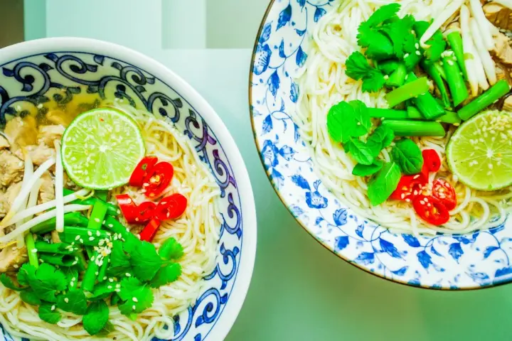Dwie miseczki aromatycznej zupy pho z makaronem, mięsem, kiełkami, limonką, chili i świeżymi ziołami.