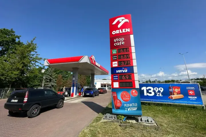 Stacja paliw Orlen z cennikiem paliw: benzyna 95 za 6.48 zł, diesel za 6.89 zł, LPG za 3.75 zł. Obok reklama hot doga i napoju.