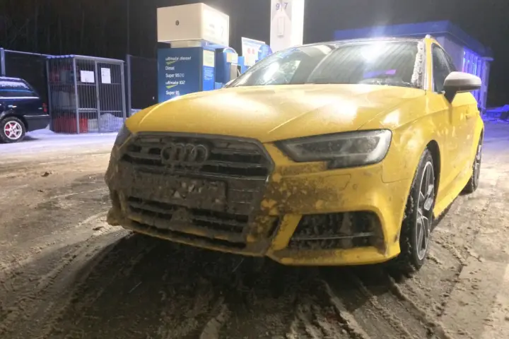 Żółte Audi na stacji benzynowej, pokryte błotem i śniegiem. Nieczytelna tablica rejestracyjna utrudnia identyfikację.