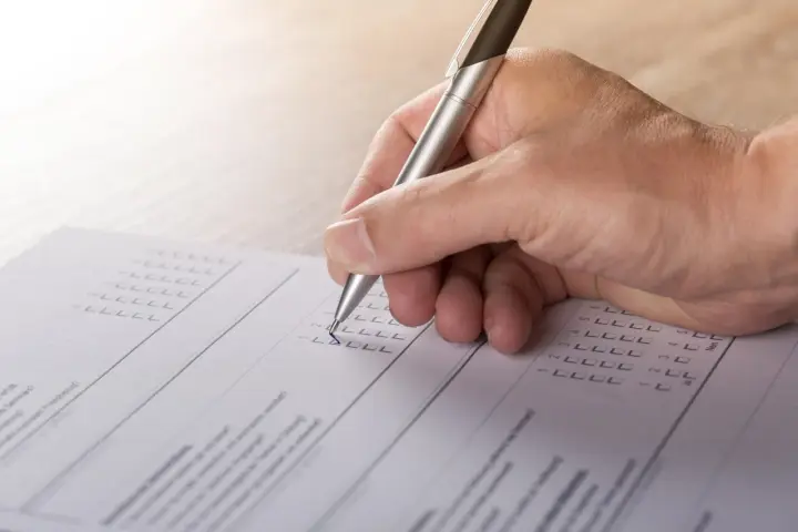 Dłoń z długopisem wypełnia formularz, zaznaczając odpowiedzi. To część procesu tworzenia wykazu majątku.