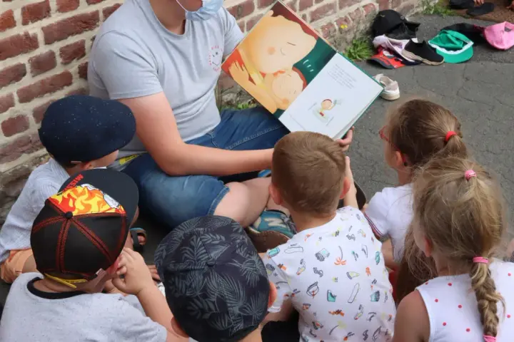 Un animateur lit un livre illustré à des enfants assis en cercle. L'image évoque un moment de partage et d'apprentissage, comme un diplôme animation.
