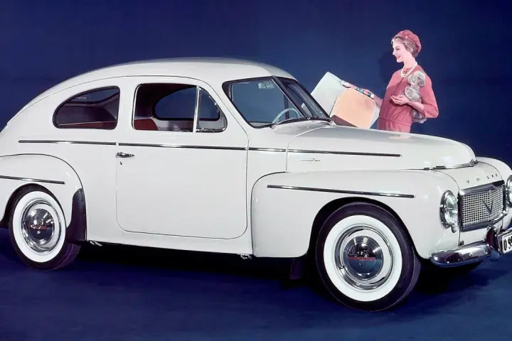 En elegant vit Volvo PV 444 med en kvinna och en hund bredvid.
