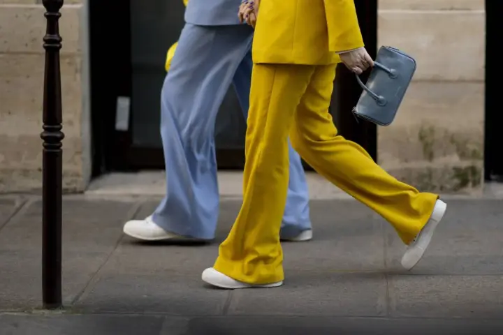 Un outfit tailleur con sneakers, giallo brillante e azzurro polvere, camminano sul marciapiede.