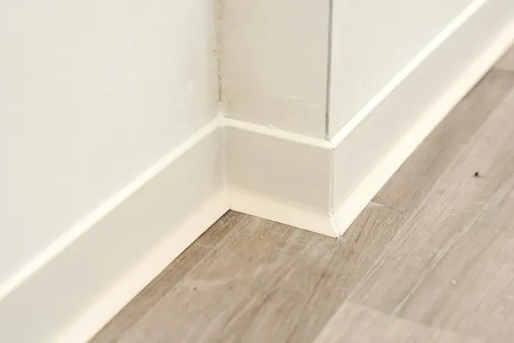 Angolo di una stanza con parquet grigio e battiscopa bianco appena installato.