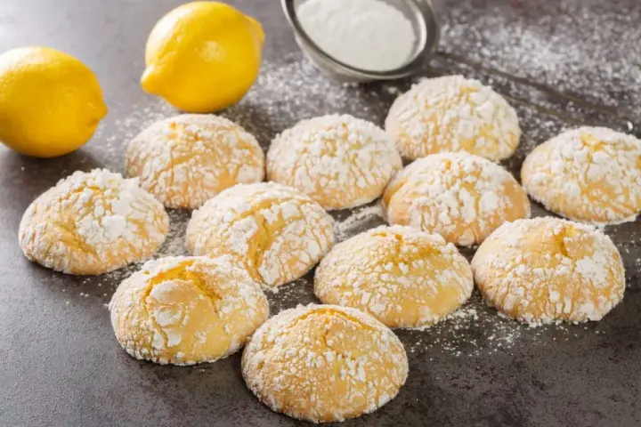 Deliziosi biscotti al limone spolverati di zucchero a velo, con limoni freschi sullo sfondo.