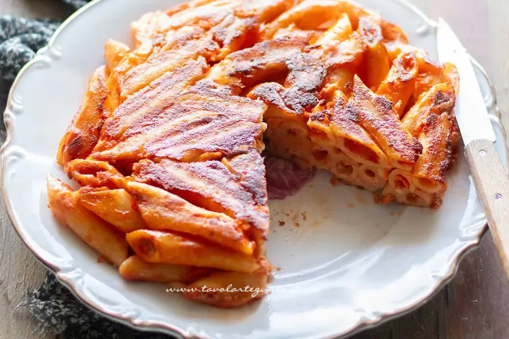 Una deliziosa frittata di maccheroni, dorata e croccante, servita su un piatto bianco con un coltello.