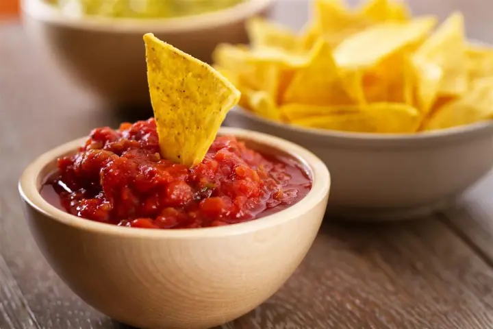 Una tortilla croccante affonda in una ciotola di fresca salsa messicana per tortillas, con altre tortillas sullo sfondo.