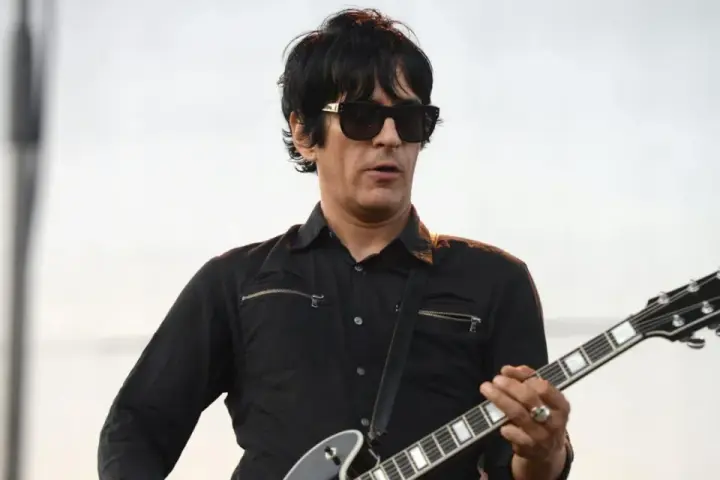 Un des membres de Eagles of Death Metal, guitariste en chemise noire et lunettes de soleil, joue sur scène.