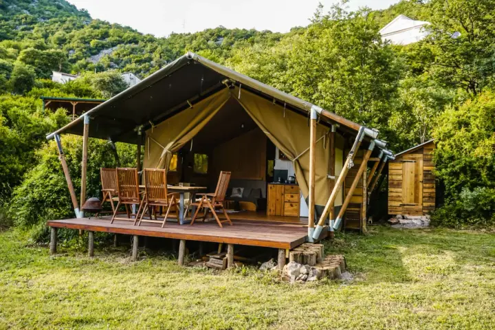Glamping w Czarnogórze: namiot z drewnianym tarasem, stołem i krzesłami, otoczony zielenią. Idealne miejsce na relaks.