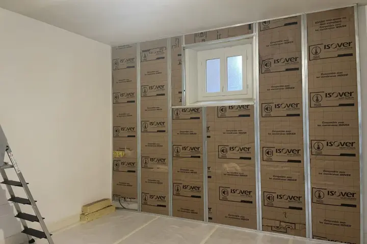 Pose de laine de verre ISOVER en 2 couches sur une structure métallique, avec une fenêtre au centre.