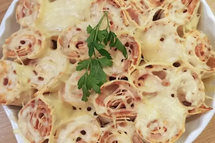 Zapiekana tortilla z szynką i ciągnącym się serem, udekorowana gałązką natki pietruszki. Pyszne danie gotowe do podania.