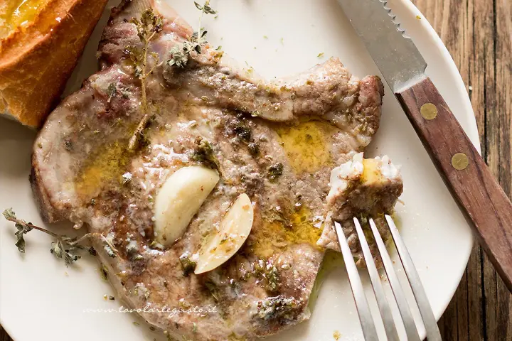Succulenta braciola di maiale condita con aglio e erbe aromatiche, servita con pane croccante.