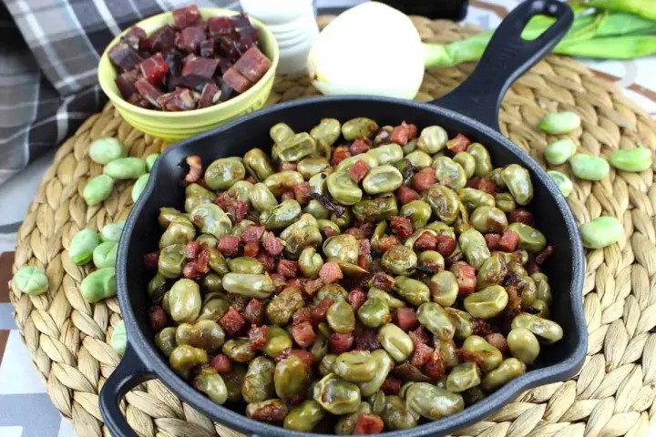 Habas tiernas salteadas con trocitos de jamón en una sartén de hierro fundido, un plato tradicional lleno de sabor.