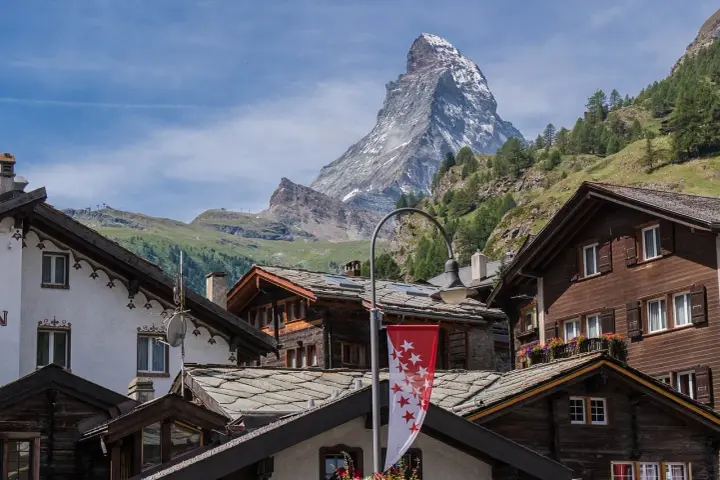Tradycyjna winieta szwajcaria: drewniane domy z kamiennymi dachami i majestatyczny Matterhorn w tle.