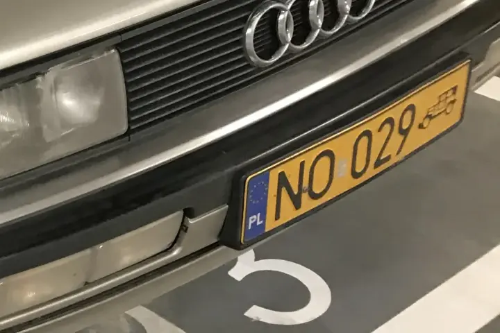 Zbliżenie na przednią część samochodu z żółtą tablicą rejestracyjną "NO 029" i logo Audi.