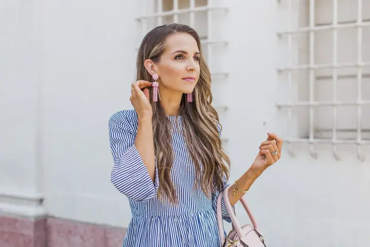 Mujer con un vestido de rayas azules y blancas, mangas acampanadas y pendientes rosas.