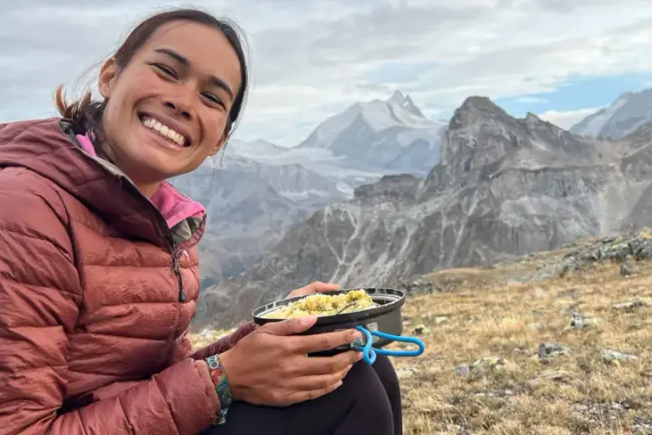 Sourire radieux d'une randonneuse savourant son repas en pleine montagne, avec des sommets enneigés en arrière-plan. Un moment de pur bonheur pour ce repas randonnée.