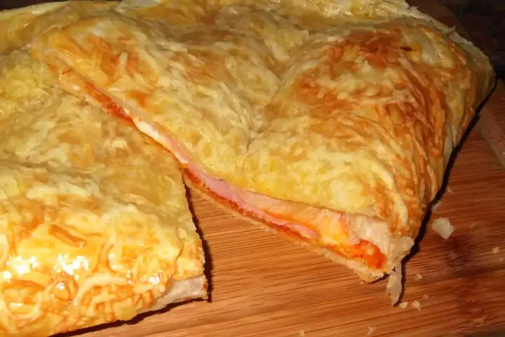 Empanada de jamón y queso dorada, con queso gratinado y relleno jugoso. ¡Un bocado delicioso!