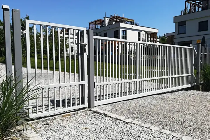 Brama z furtką bez słupka, otwarta na posesję z nowoczesnymi budynkami.