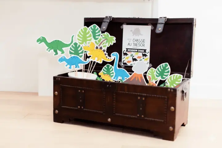 Coffre en bois rempli de décorations de dinosaures et de feuilles tropicales.