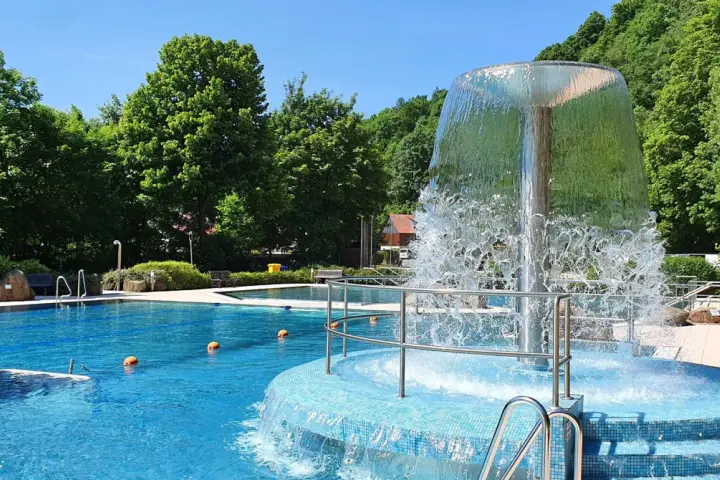 Erfrischender Brunnen im Naturbad Elbingerode, umgeben von grünen Bäumen und blauem Wasser.
