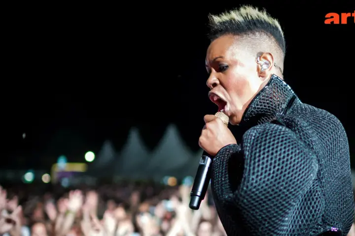 Skunk Anansie en pleine performance, micro d'or à la main, devant une foule en délire. La chanteuse captive avec son énergie.