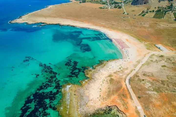 Widok z lotu ptaka na turkusowe morze i piaszczyste bari plaże z rzędami parasoli.