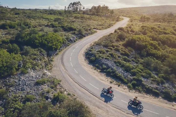 Due moto KTM sfrecciano su una strada tortuosa tra colline verdi. Un'avventura che celebra il KTM Connect.