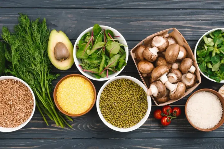 Variedad de alimentos ricos en proteinas vegetales: aguacate, hinojo, lentejas, champiñones, arroz, tomates y hojas verdes.