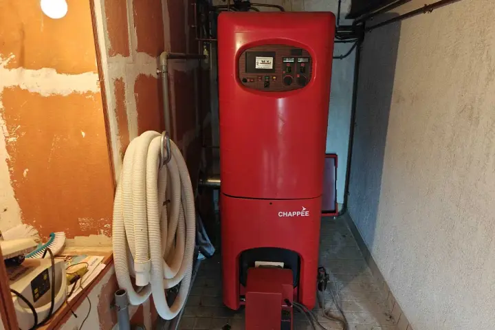 Chaudière rouge Chappée dans une pièce. Un tuyau blanc enroulé est accroché au mur. Pensez à l'assurance chaudière pour votre confort.
