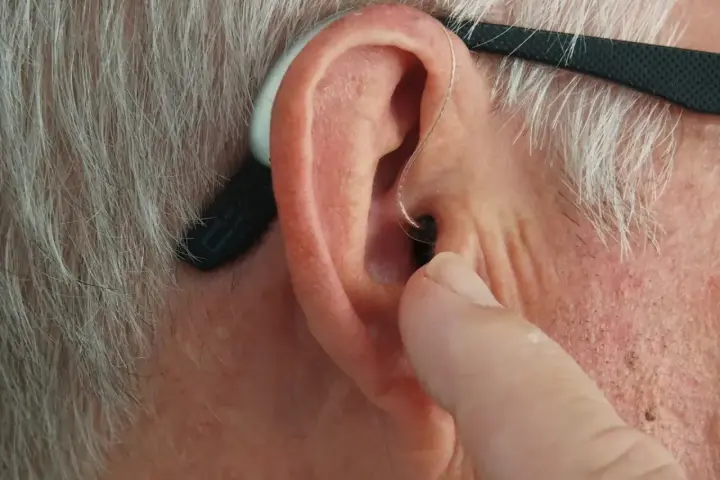 Palec wskazujący dotyka ucha, na którym widoczny jest aparat słuchowy. Zastanawiasz się, dlaczego aparat słuchowy piszczy?