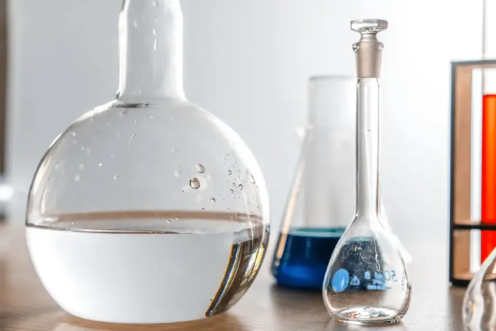 Laboratorieglas med vatten och blå vätska. Frågan om man kan dricka destillerat vatten är relevant i vetenskapliga sammanhang.