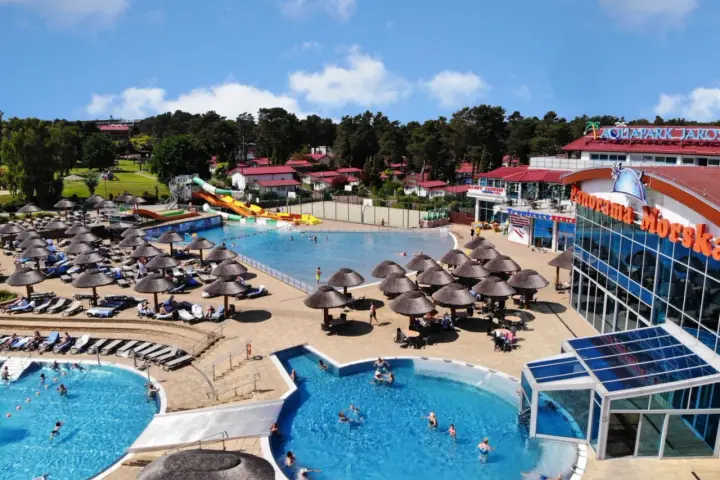 Aquapark w Jarosławcu: baseny, zjeżdżalnie i leżaki pod parasolami. Wiele osób korzysta z atrakcji, tworząc radosną atmosferę.