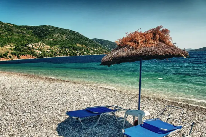 Plaża z leżakami i parasolem, w tle zielone wzgórza i turkusowe morze. To idealne miejsce na wypoczynek na grupie wysp na Morzu Egejskim.