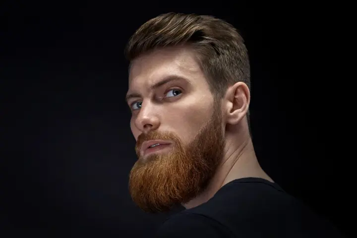 Hombre con barba rojiza y peinado actual, con el pelo peinado hacia atrás y un corte moderno.