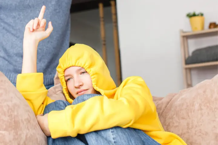 Ein Teenager in gelbem Hoodie zeigt seiner Mutter den Mittelfinger. Er hat keinen Respekt vor ihr.