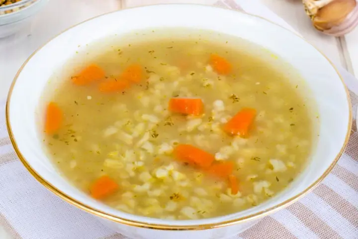 Aromaticzna zupa na rosole z makaronem i marchewką, podana w białej miseczce ze złotym rantem.