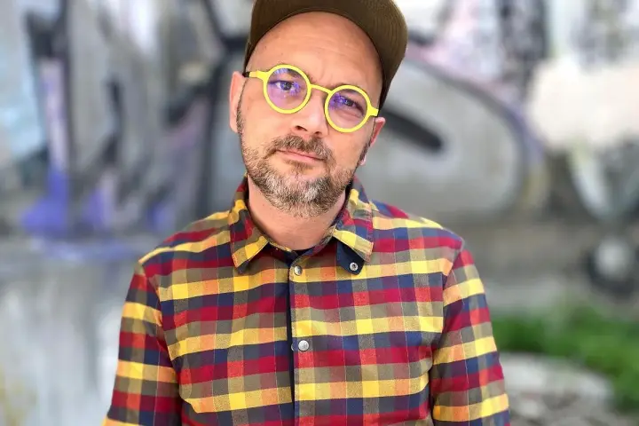 Filip Springer w okularach i koszuli w kratę, na tle graffiti.