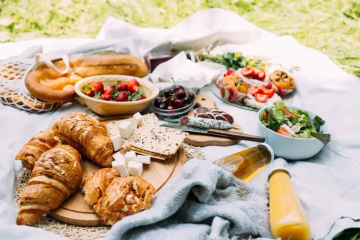 Pyszne jedzenie na piknik: świeże pieczywo, owoce, sałatka, sery i napoje.