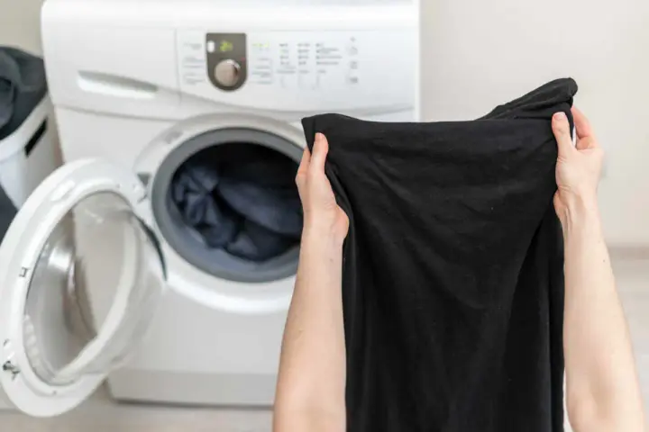Mani che tengono capi neri, pronti per essere messi nella lavatrice aperta.