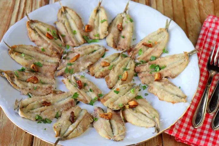 Un plato blanco con boquerones fritos, dorados y crujientes, espolvoreados con perejil fresco y trocitos de ajo.