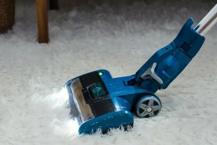 Blauer Staubsauger mit LED-Licht reinigt flauschigen Teppich. Die Leistung, wie viel Watt hat ein Staubsauger, ist entscheidend für die Saugkraft.
