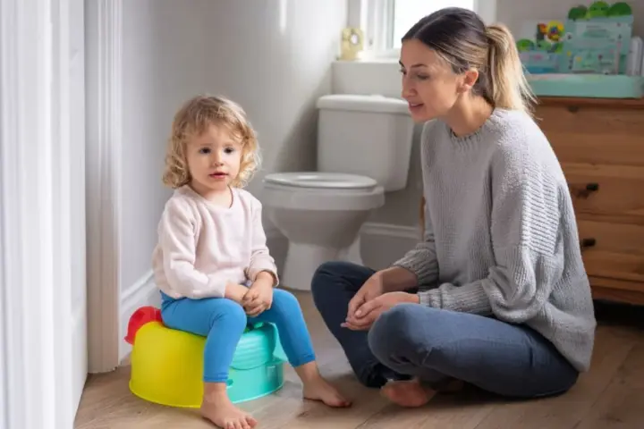Mama uczy dziecko korzystać z nocnika. Mała dziewczynka siedzi na kolorowym nocniku, a mama siedzi obok, wspierając ją.