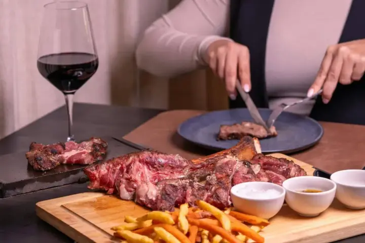 Idealne **jakie wino do wieprzowiny**? Czerwone wino i soczysta wieprzowina na desce, z frytkami i sosami.