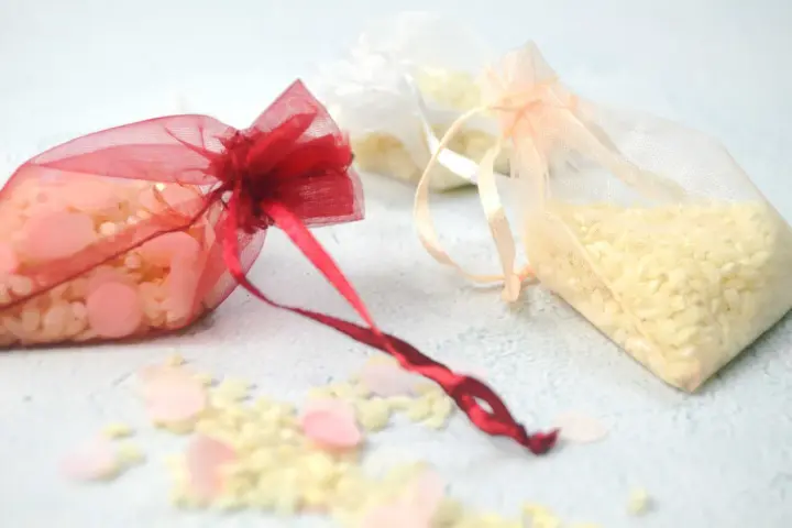 Bolsitas de organza rojas, blancas y melocotón llenas de arroz, listas para usarse como recuerdo. Ideas para como hacer bolsitas de arroz para bodas.