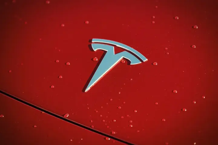 Błyszczące logo Tesli na czerwonej karoserii z kroplami deszczu. Czy Tesla jest tylko elektryczna?