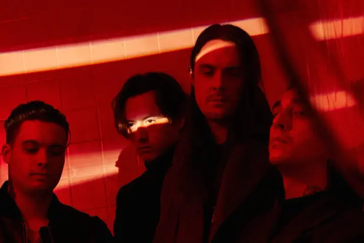 Les membres de Bad Omens posent dans une ambiance rouge intense, éclairés par des ombres dramatiques.