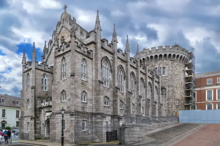 Kamienne mury i strzeliste wieże zdobią zamek w Dublinie. Gotycka architektura i chmurne niebo tworzą majestatyczny widok.