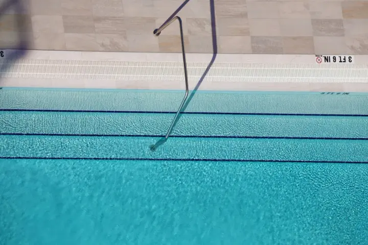 Escalera metálica en piscina de agua clara, con marcas de profundidad. El mantenimiento de piscinas es clave para su disfrute.